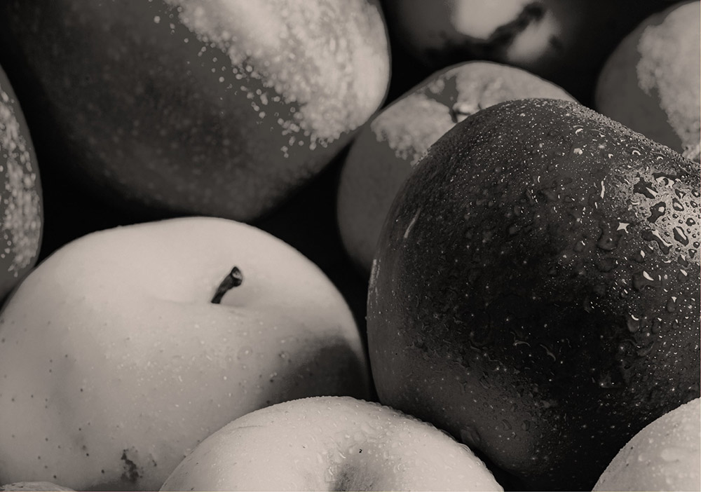 Nahaufnahme von mehreren Äpfeln mit Wassertropfen auf der Oberfläche, in Schwarz-Weiß dargestellt.