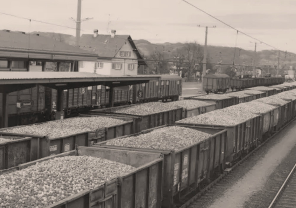 Mehrere mit Äpfeln beladene Güterzugwaggons sind auf parallelen Gleisen neben einem kleinen Bahnhofsgebäude abgestellt.